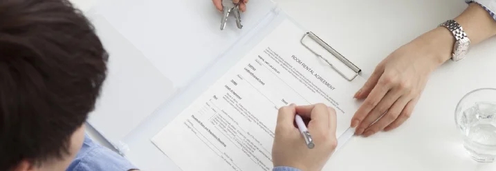 Eine Person unterschreibt einen Mietvertrag mit einem Stift auf einem Schreibtisch.